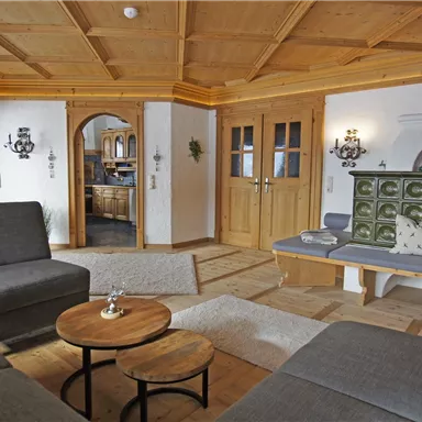 Ein gemütliches Wohnzimmer mit holzverkleideten Wänden und einem offenen Raumkonzept. Moderne Möbel und ein traditioneller Ofen schaffen eine einladende Atmosphäre.