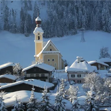 A picturesque winter landscape with snow-covered cottages and a church. The trees are covered in snow, and the surroundings radiate tranquility.