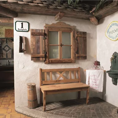 Ein gemütlicher Eingangsbereich mit einer Holzbank und einem Fenster. Die Wände sind dekorativ gestaltet und es gibt eine kleine Wandbrunnen.