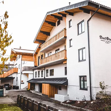 A modern, multi-story building with wooden cladding in a rural setting. The garden is well-maintained and surrounded by trees.