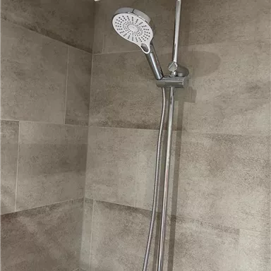 Eine moderne Dusche mit einer großen Regendusche und einer Handbrause. Die Wände sind mit braunen Fliesen verkleidet.