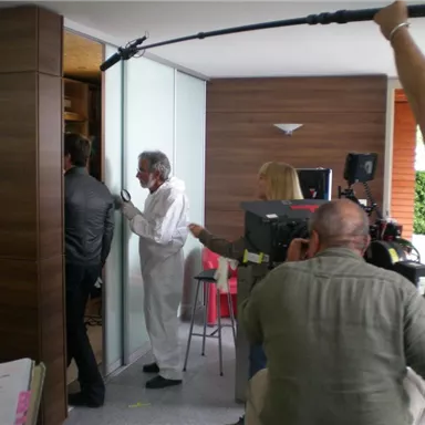 Eine Filmaufnahme in einem modernen Raum. Ein Team mit Kameras und Schauspielern ist bei der Arbeit.