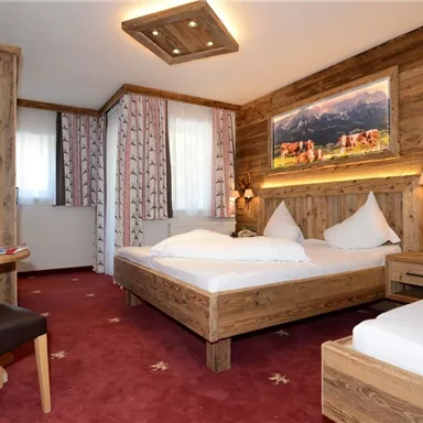 Ein gemütliches Hotelzimmer mit Holzmöbeln und roten Teppichboden. Es gibt zwei Betten, einen Schreibtisch und Fenster mit Vorhängen.