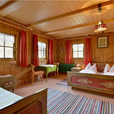 Ein gemütliches Zimmer mit Holzverkleidung und roten Vorhängen. Es gibt zwei Betten, einen Tisch und einen Teppich.