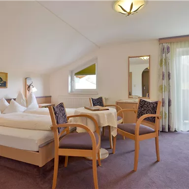 Ein gemütliches Hotelzimmer mit zwei Betten, einem Tisch und Stühlen. Große Fenster sorgen für viel Licht.