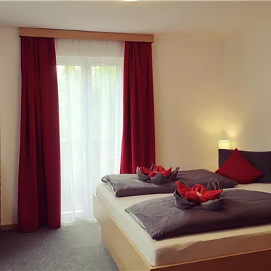 Ein gemütliches Zimmer mit zwei Einzelbetten und roten Vorhängen. Die elegante Einrichtung sorgt für eine einladende Atmosphäre.