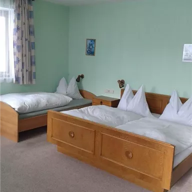 A simple bedroom with two beds. The walls are light green and there are windows with curtains.