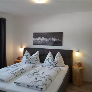 Ein gemütliches Schlafzimmer mit einem Doppelbett und modernen Holzmöbeln. Die Wände sind hell und dekoriert mit einem Landschaftsbild.