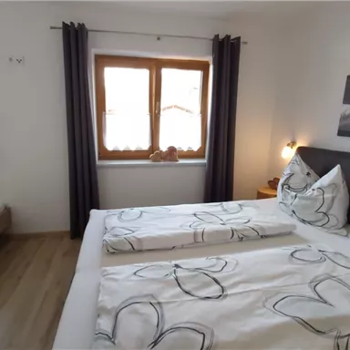 Ein gemütliches Schlafzimmer mit zwei Betten und hellen Fenstern. Die Wände sind in neutralen Farben gehalten und es gibt dekorative Bettwäsche mit Blumenmuster.