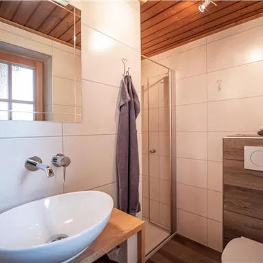 Ein modernes Badezimmer mit einer Dusche, einem Waschbecken und Holzdetails. Es gibt eine Fensterfront, die natürliches Licht hereinlässt.