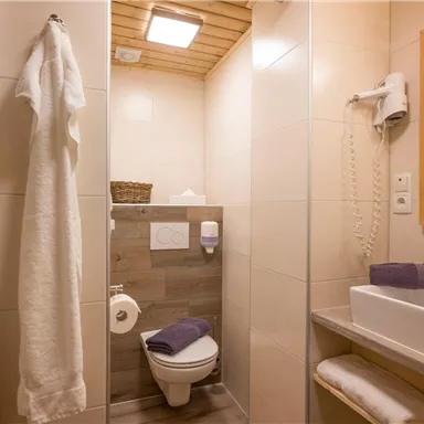 Ein modernes Badezimmer mit hellen Fliesen und Holzdetails. Es gibt ein Waschbecken, eine Toilette und Handtücher in sanften Farben.