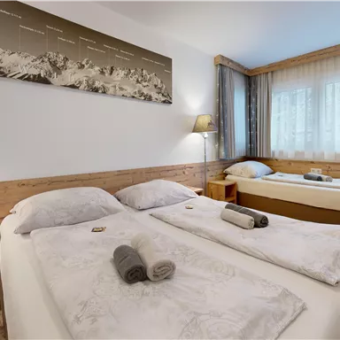 A cozy room with two single beds and an additional bed. The decor is modern with wooden elements and plenty of natural light.