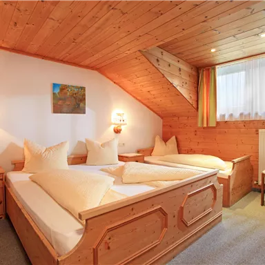 Ein gemütliches Zimmer mit Holzverkleidung und zwei Betten. Am Fenster gibt es einen Ausblick auf das Tageslicht und eine kleine Kunstleinwand an der Wand.