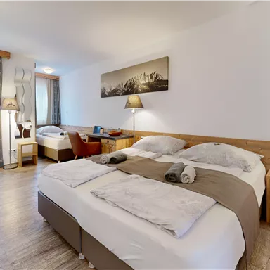 A cozy hotel room with a large double bed and wooden furniture. The windows provide daylight and there are decorative lamps as well as a picture on the wall.
