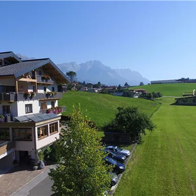 A picturesque house in the mountains with green meadows and a clear sky. The mountains are visible in the background.