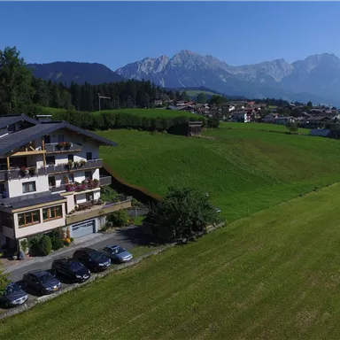 A beautiful farm with a view of the mountains and a spacious meadow. In the foreground, several cars are parked in a parking lot.