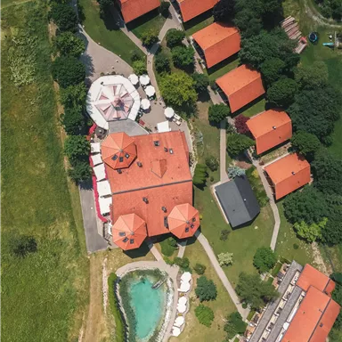 Ein Luftbild eines Wohngebiets mit roten Dächern und einem kleinen Teich. Umgeben von grünen Flächen und Bäumen.