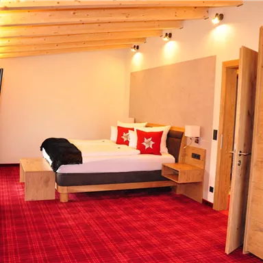 A cozy bedroom with a double bed and a red plaid carpet. The walls are bright, and there are modern furniture and lighting.