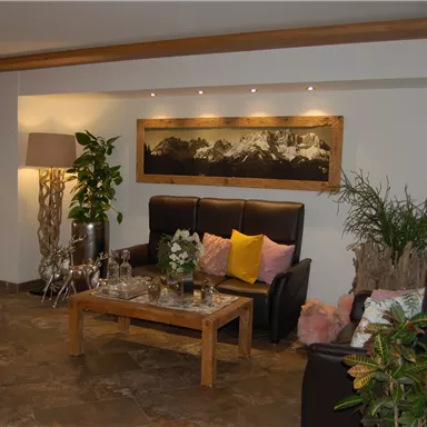 Ein gemütlicher Wohnbereich mit zwei Sesseln und einem Holztisch. Die Wände sind geschmückt mit Pflanzen und einem großen Bild.