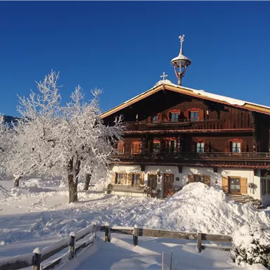 A picturesque wooden house in the snow, surrounded by frosty trees. The clear blue sky complements the winter landscape.