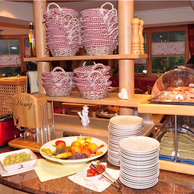 A buffet with various foods and drinks. On top, there is a basket with food, and below, a plate with fresh fruit.