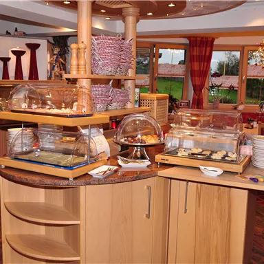 An inviting buffet area with various dishes under glass covers. The warm wooden decor and large windows create a cozy atmosphere.
