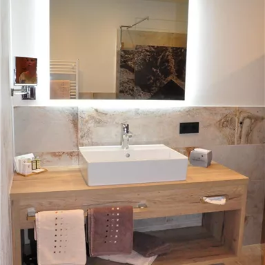 A modern bathroom with a stylish sink on a wooden shelf. The walls are in neutral tones and there are decorative towels.