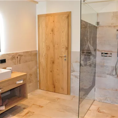 A modern bathroom with a glass shower and a wooden dresser. Bright tiles and a large mirror create an inviting atmosphere.