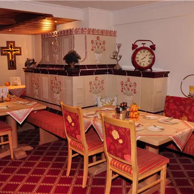 A cozy restaurant with wooden furniture and red upholstered benches. The walls are cheerfully decorated and a large clock creates an inviting atmosphere.