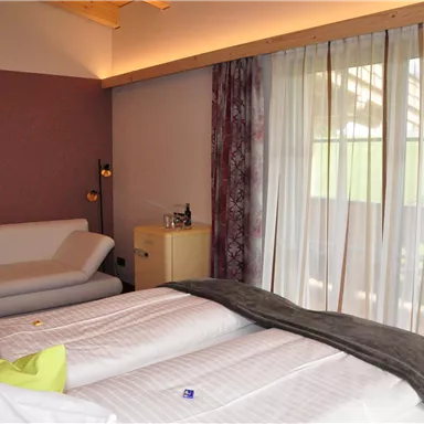 A cozy bedroom with two beds and a comfortable sofa. Large windows let in plenty of light and offer a view outside.