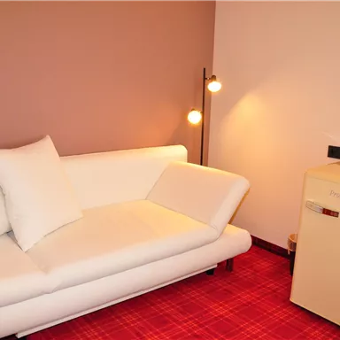 A cozy room with a white sofa and a floor lamp. Next to the sofa is a small refrigerator.