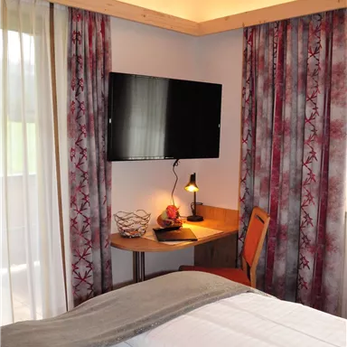 A cozy room with a double bed and a television. The space is bright and modernly furnished, with decorative window trim.