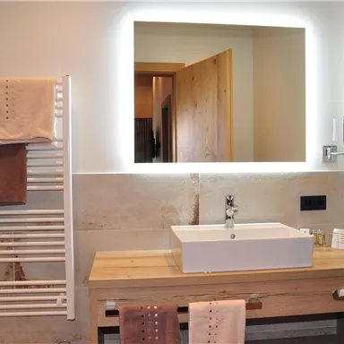 A modern bathroom with a rectangular basin and a lighted mirror. Towels are hanging on a towel holder made of white steel.