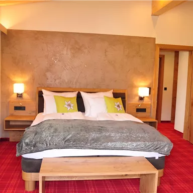A cozy room with a double bed and wooden details. The walls are light and there is a red carpet.