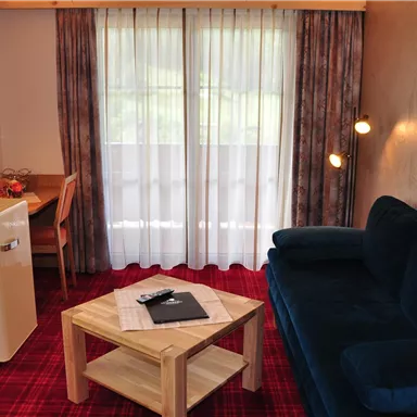 A cozy room with a blue sofa, a table, and a refrigerator.  
Large windows let in plenty of light and create a pleasant atmosphere.