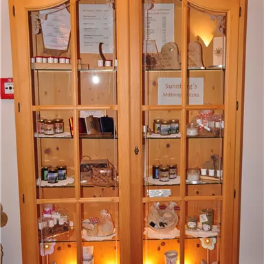 A wooden cabinet with a glass front that displays various cosmetic products and care items. Inside, the products are well-lit and neatly arranged.
