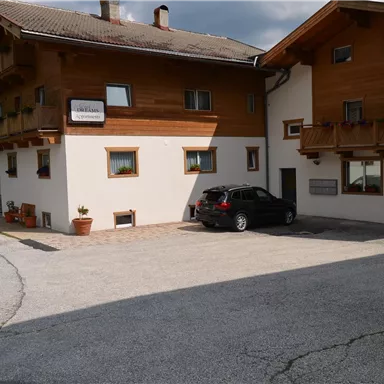 Ein rustikales Holzhaus mit einem Parkplatz und mehreren Fenstern. Der Himmel ist teilweise bewölkt.