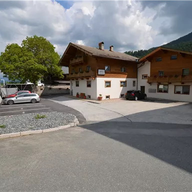 Eine gemütliche alpine Unterkunft mit einem großen Parkplatz. Umgeben von grünen Hügeln und bewölktem Himmel.