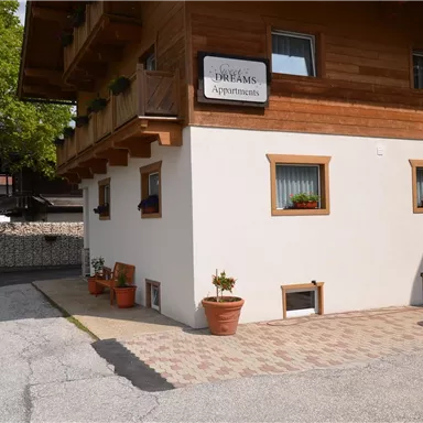 Ein modernes Gebäude mit Holzverkleidung und weißen Wänden. Vor dem Haus stehen Töpfe mit Pflanzen und ein schwarzes Auto parkt auf dem Platz.