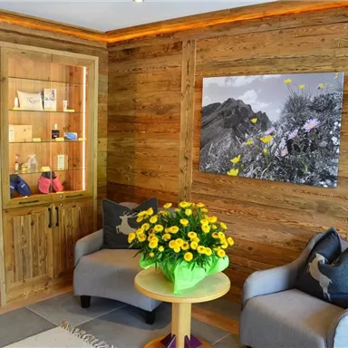 Ein einladender Raum mit holzvertäfelten Wänden, zwei gemütlichen Sesseln und einem runden Tisch. Auf dem Tisch steht ein Blumenstrauß und an der Wand hängt ein Schwarz-Weiß-Bild mit bunten Blumen.