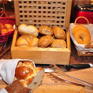 A selection of fresh rolls and croissants in baskets on a table. Next to the bread is a cutlery set and a shiny red toaster.