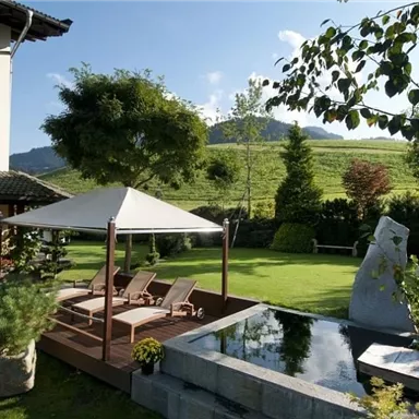 A beautiful garden with loungers and a water feature. In the background, green hills and trees are visible.