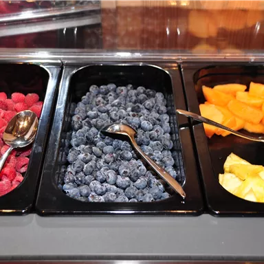 A selection of fresh fruits in bowls. Featured are raspberries, blueberries, melons, and pineapples.