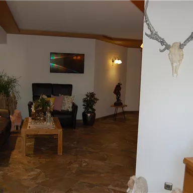 Ein gemütlicher Eingangsbereich mit bequemen Sesseln und einem Holztisch. An den Wänden sind Pflanzen und dekorative Elemente in warmen Farben.