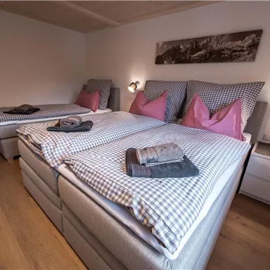 Ein gemütliches Schlafzimmer mit drei Betten und karierten Bettdecken. Die Wände sind hell gestrichen und es gibt moderne Nachttischlampen.