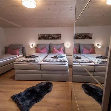 Ein modernes Schlafzimmer mit mehreren Betten und gemütlicher Einrichtung. Es gibt helle Wände, sanfte Beleuchtung und einen warmen Holzfußboden.