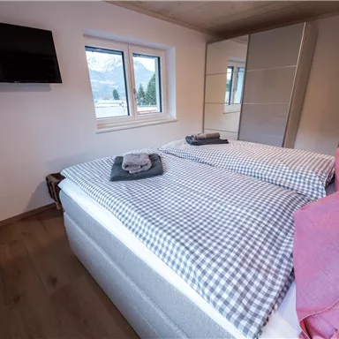 Ein modernes Schlafzimmer mit zwei Einzelbetten und gestreiften Bettdecken. Fenster lassen viel Tageslicht herein und es gibt einen Fernseher an der Wand.