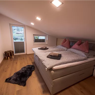 Ein gemütliches Schlafzimmer mit einem Doppelbett und zwei Kissen. Große Fenster sorgen für Tageslicht, und der Fußboden ist aus Holz.