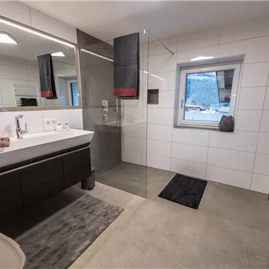 Ein modernes Badezimmer mit einer Glasdusche und einer breiten Waschbeckenanlage. Helle Fliesen und dunkle Möbel sorgen für einen eleganten Look.