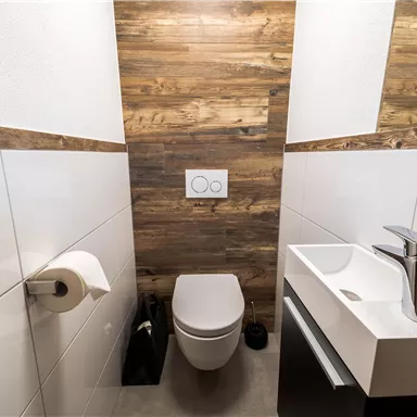 Ein modernes Badezimmer mit Holzverkleidung und eleganten sanitären Anlagen. Es enthält ein WC, ein Waschbecken und eine Toilettenpapierhalterung.